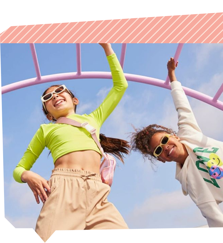Two girls hanging and laughing on playground monkey bars against a blue sky