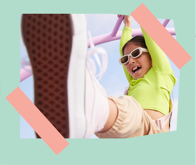 Girl in sunglasses hanging from playground monkey bars, sneaker in foreground